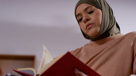 Mujer-Musulmana-Con-Hijab-Sentada-En-Un-Sofá-En-Casa-Leyendo-O-Estudiando-El-Corán-1